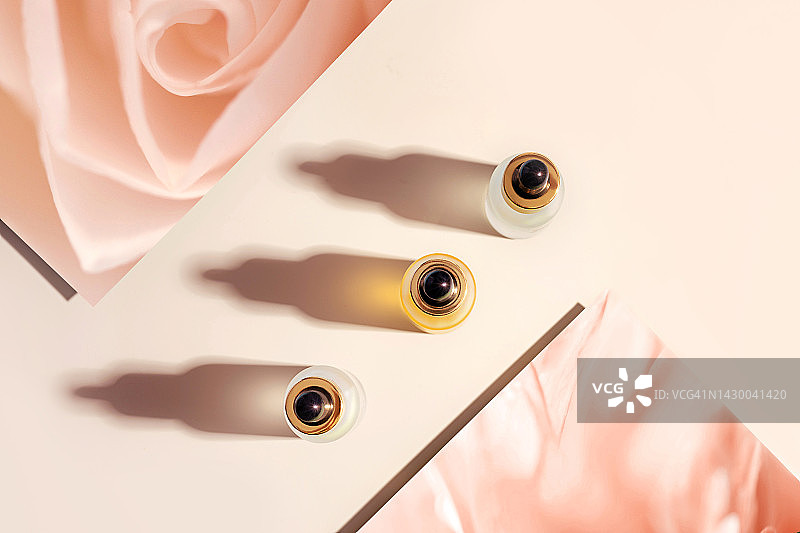 面部皮肤护理步骤：面部精华液或精油和茶玫瑰花，粉米色背景图片素材