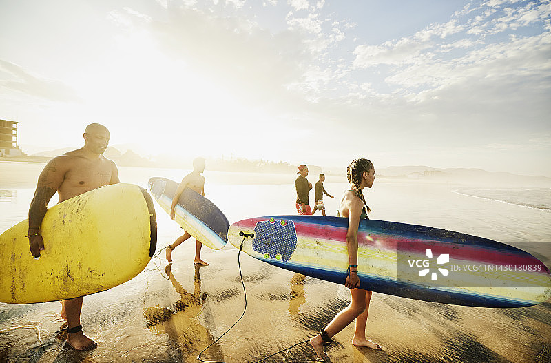 一家人在冲浪课程中将冲浪板抬入海中的远景图片素材