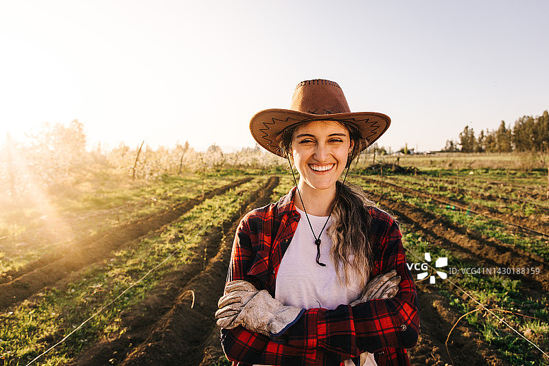 在农田里双臂交叉的微笑女农民。肖像照。垄沟土壤。图片素材