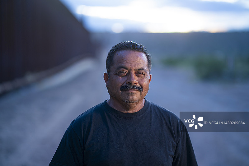 自信的墨西哥男人站在新墨西哥州和华雷斯之间的边境墙旁图片素材