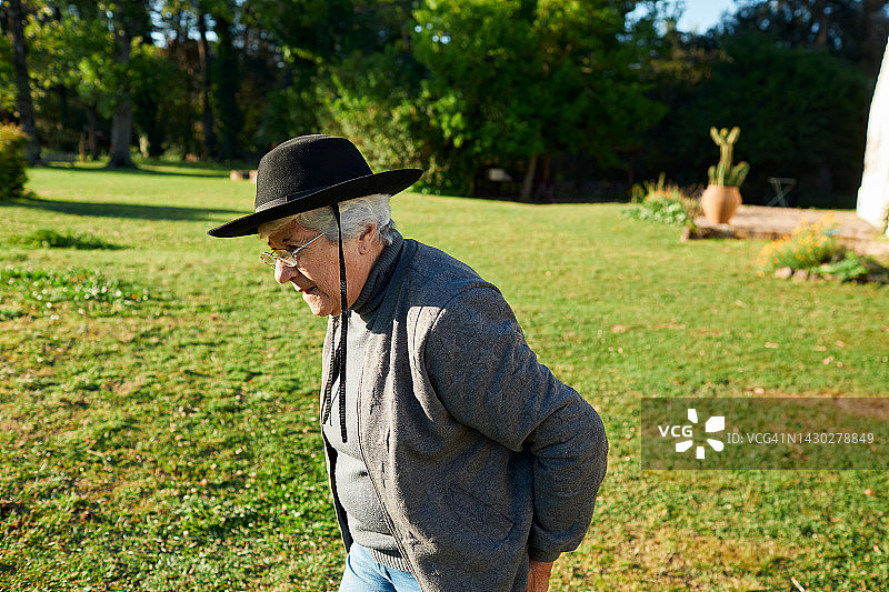一位年长的白人妇女在草地上行走，远离牧场住宅图片素材