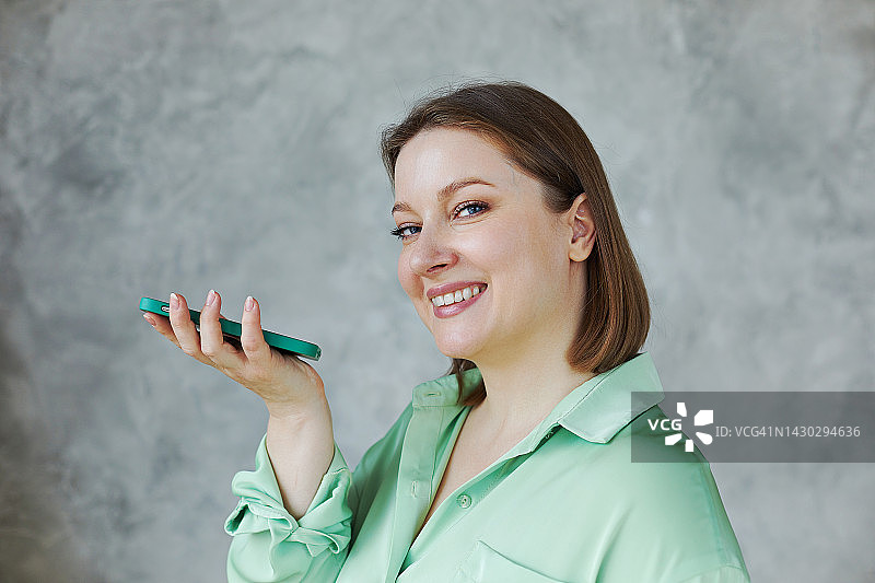 在灰色背景墙上用扬声器打电话的迷人加大码女子图片素材