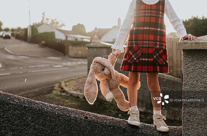 小女孩拿着毛绒玩具兔子在墙上保持平衡图片素材