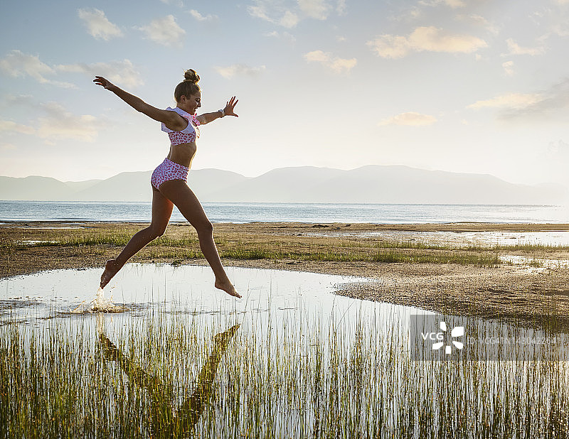 穿比基尼的少女（14-15岁）在日出时跳跃于湖面之上图片素材