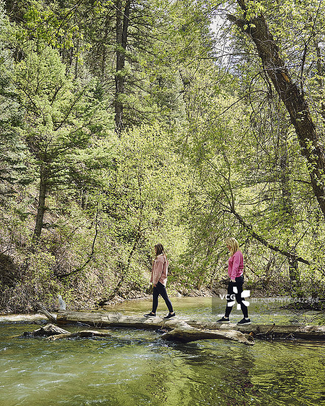 母亲和女儿（12-13岁）在湖上原木上行走图片素材