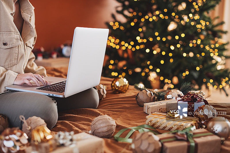 年轻女人在笔记本电脑上工作，屏幕显示圣诞新年装饰的客厅内景图片素材