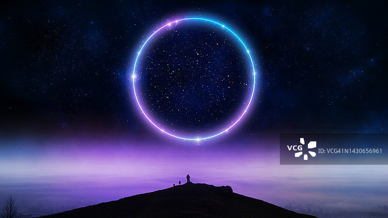 一个神秘的概念，一个人站在小山上，夜空中有一个发光的霓虹灯圈传送门。远处是雾蒙蒙的冬季景观。图片素材