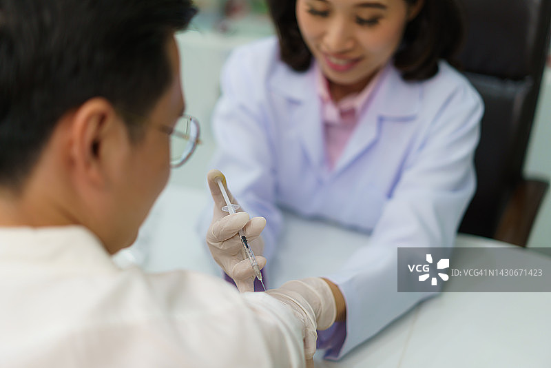 自信的亚洲女药剂师准备为一名男子接种疟疾、破伤风、伤寒、肝炎疫苗图片素材