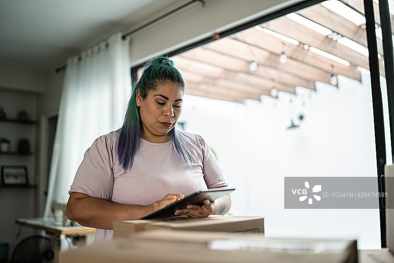 中年女人在家使用平板电脑检查纸箱图片素材