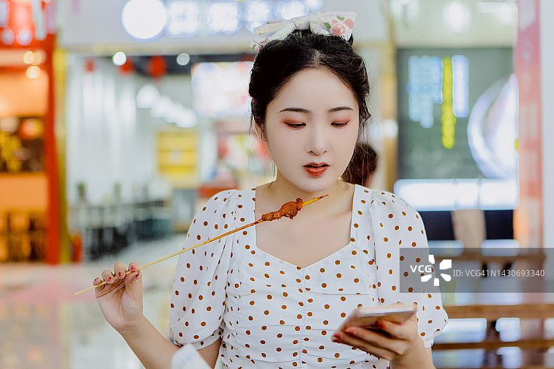 在购物中心享受夜生活，吃烤肉串玩手机的女人图片素材