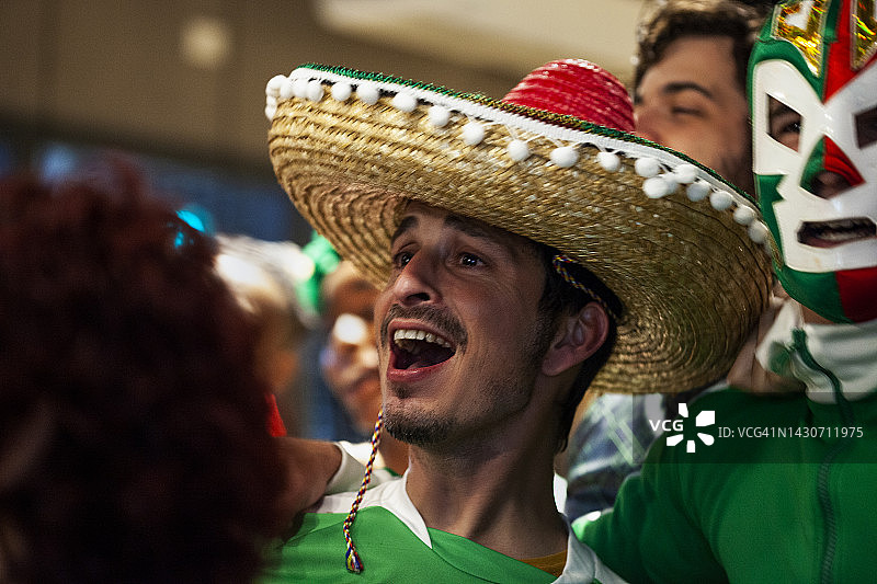 一群年轻的墨西哥体育迷在拥挤的酒吧里戴着墨西哥帽和摔跤面具图片素材