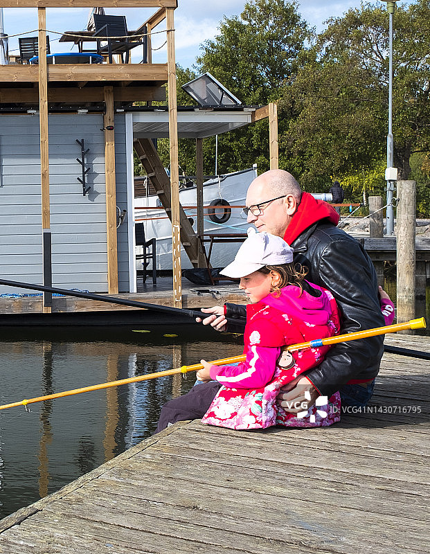 在湖上钓鱼的白人家庭：一个男人和一个7岁的女孩正在用钓鱼线钓鱼图片素材