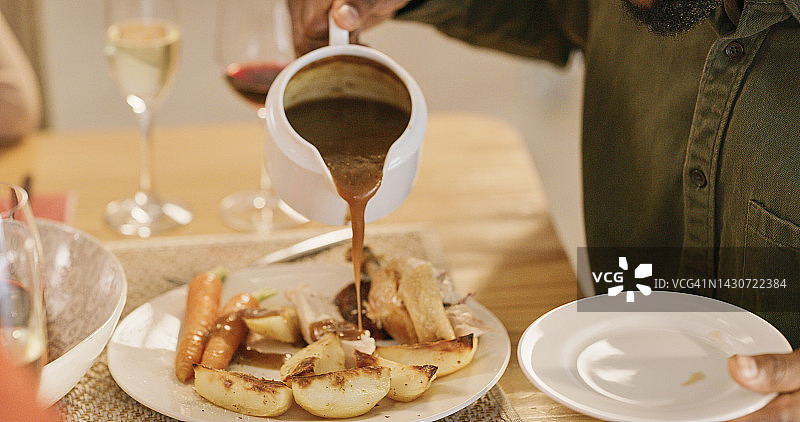 手在餐桌上为家庭晚餐倒酱汁和土豆图片素材