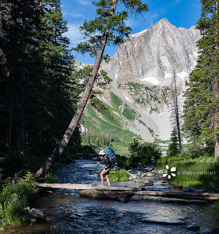 背着背包，走过原木桥，离开雪堆湖的中年妇女。在栗色钟附近进行的四程背包旅行。阿斯彭，科罗拉多州。图片素材