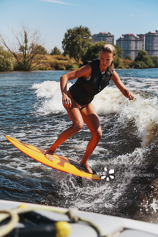 年轻漂亮女子玩尾波冲浪，手持亮橙色板图片素材