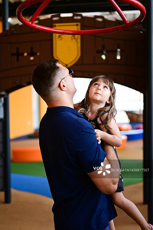 游乐园里和爸爸在一起的3岁女孩，父亲帮助女儿在操场上玩耍图片素材