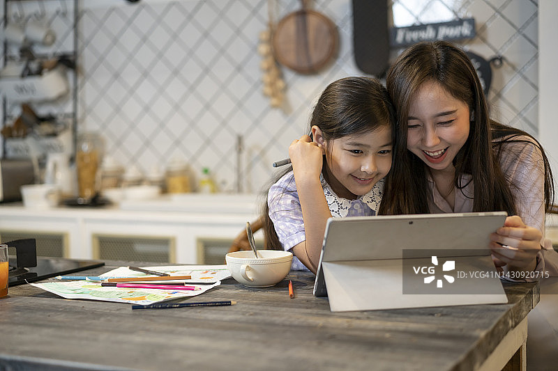 年轻的亚洲母亲在桌子上准备了健康的早餐，在家教育她的女儿并帮助她完成学校作业图片素材