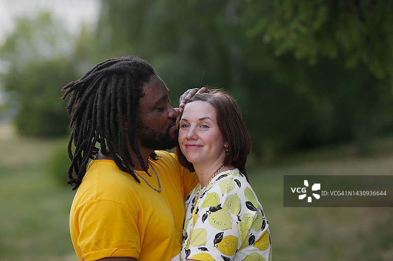 中年国际夫妇在夏日公园里拥抱，男人亲吻女人图片素材