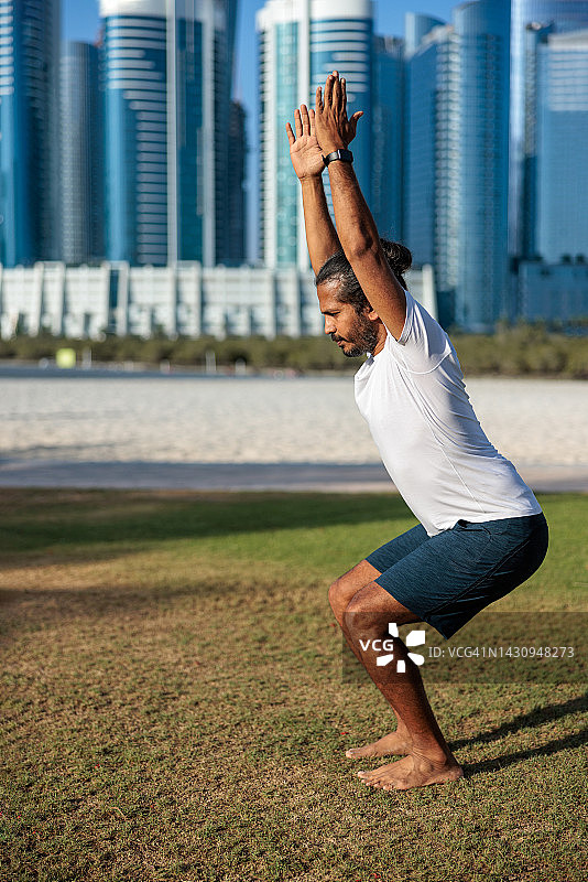 在阿布扎比公园草坪上做瑜伽椅子式伸展的男人图片素材