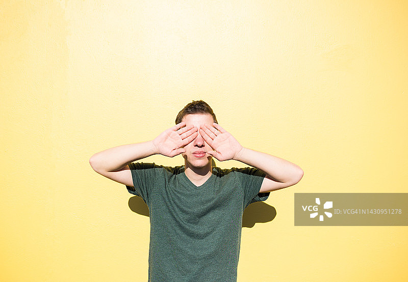 站在黄色墙前，用手遮住眼睛的男人肖像图片素材