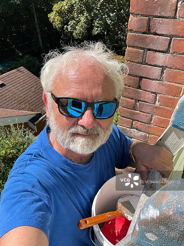 在加拿大不列颠哥伦比亚省，站在梯子上粉刷房屋的年长男人肖像图片素材