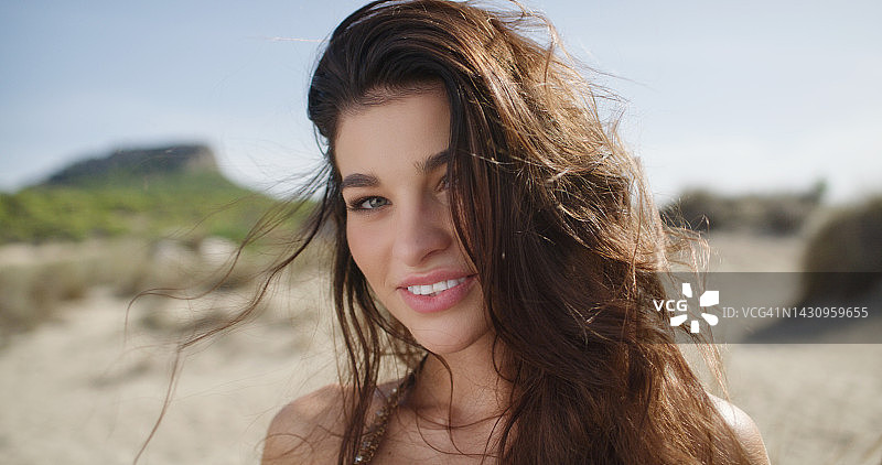 年轻漂亮的女孩笑着看向镜头，长长的棕色头发在风中飘动图片素材