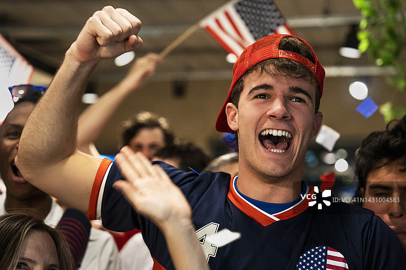 在拥挤的酒吧里庆祝美国队在体育赛事中获胜的年轻男人图片素材