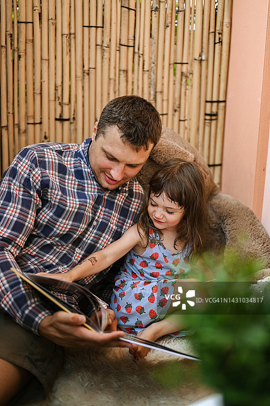 年轻的父亲和蹒跚学步的女儿一起读书，享受亲子时光图片素材