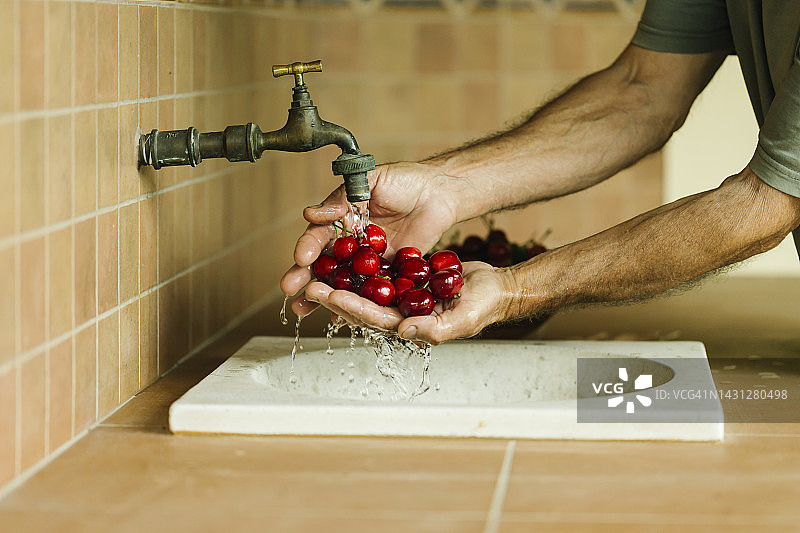年长的男人在乡村厨房用水清洗新鲜的红色有机樱桃——健康生活方式和有机水果概念图片素材