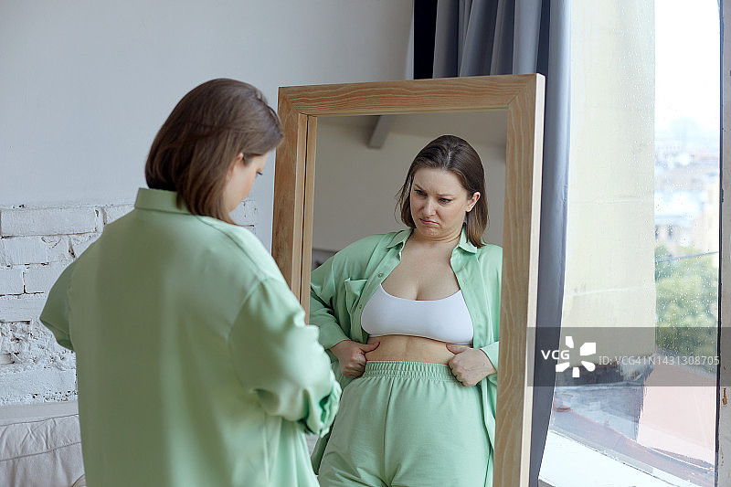 看着镜子中身材发福的自己，感到沮丧和不满的加大码女士图片素材