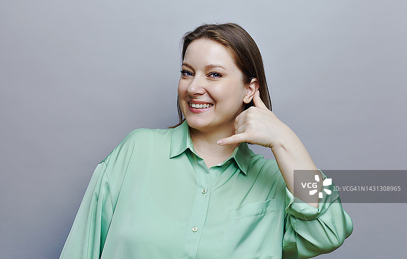 灰色背景上摆姿势的超大号女人拿着呼叫我回来的牌子图片素材