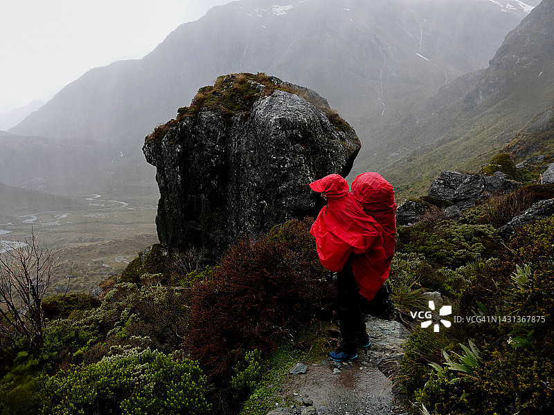 穿着雨具的背包女人看着倾盆大雨和强风，靠近新西兰哈里斯峰图片素材