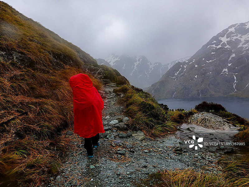 穿着雨具的背包女人看着倾盆大雨和强风，靠近新西兰哈里斯峰图片素材