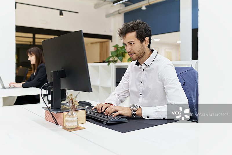 年轻人坐在电脑前工作，椅背上放着外套图片素材