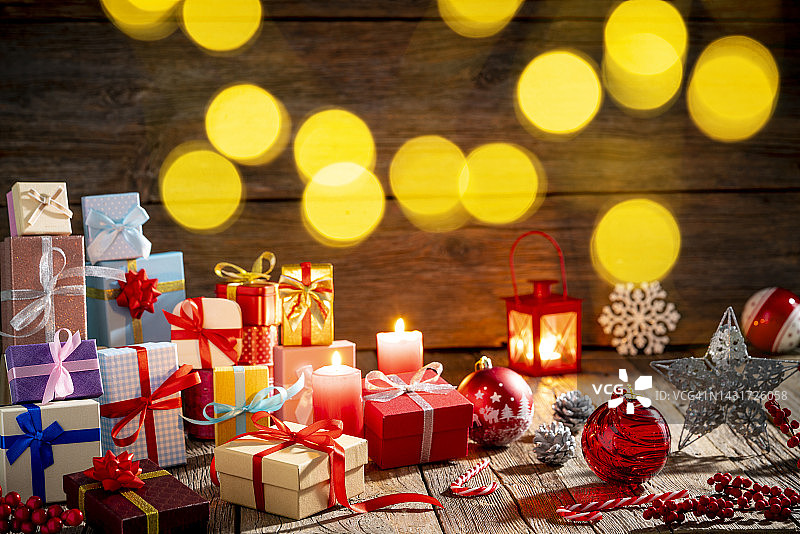 圣诞节时，许多礼品盒堆放在带有圣诞灯和灯笼的木质背景上图片素材