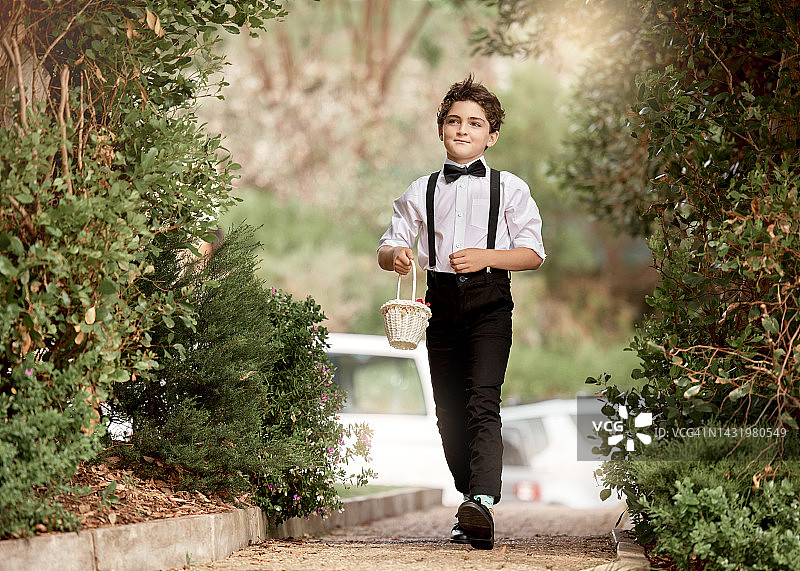 快乐的男孩拿着花篮参加婚礼，并将玫瑰花瓣撒在地板上图片素材