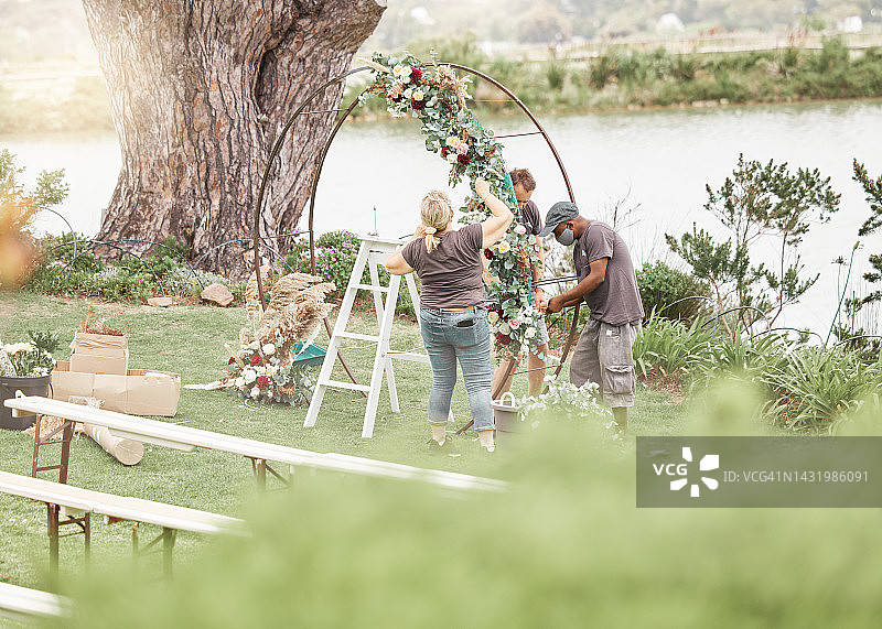 婚礼仪式：花艺师在宁静美丽的湖边用鲜花装饰拱门图片素材