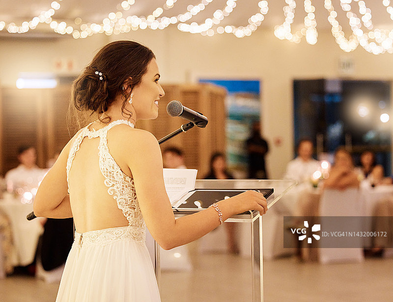 婚礼演讲：新娘手持麦克风向婚宴来宾致辞。已婚女人在宴会上向亲朋好友讲述幸福的爱情故事。图片素材