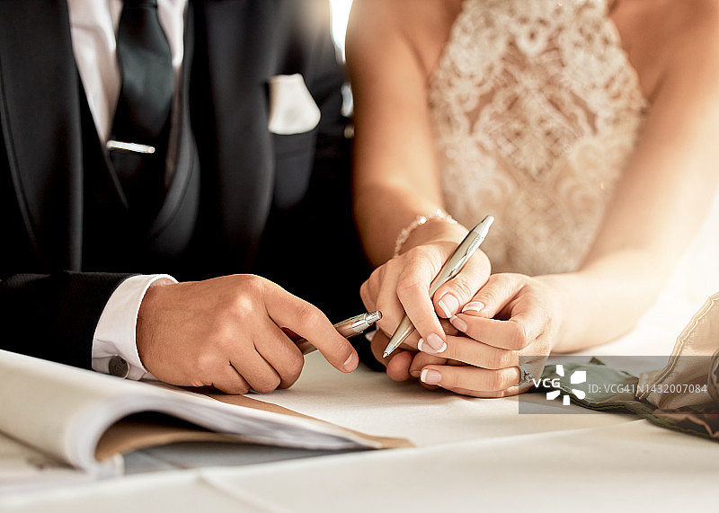 夫妇签署结婚证书，进行结婚登记，并签署法律结合的文件。新娘、新郎的特写镜头以及为庆祝爱情、承诺和协议而书写合同的双手图片素材
