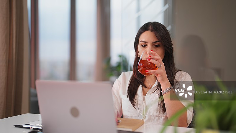 年轻女人使用笔记本电脑时小憩片刻，喝点东西图片素材