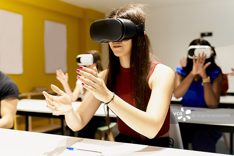 戴着VR眼镜移动双手的长发红衣女子，背景中还有其他戴VR眼镜的女子图片素材