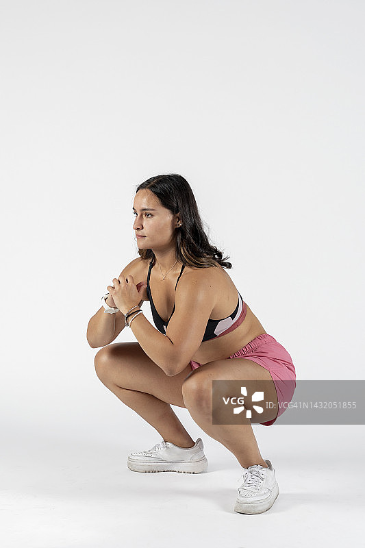 在白色背景的演播室里做深蹲的运动装运动员图片素材