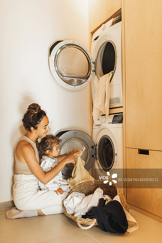 母女一起将待洗衣物放入洗衣机，可持续育儿图片素材