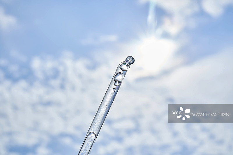 蓝色天空背景上带精华液、精油或玻尿酸凝胶的化妆品滴管，适用于广告宣传图片素材