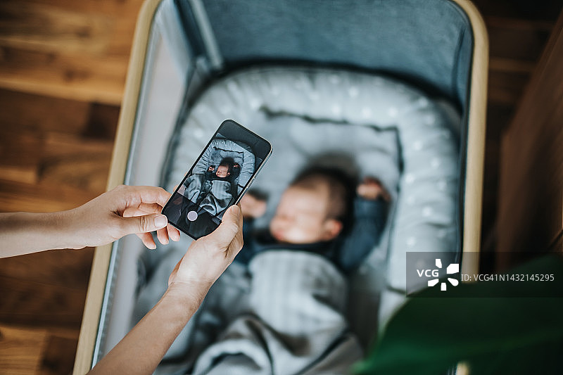 亚洲母亲在家用手机拍摄熟睡的新生女婴，记录新生活，分娩回忆，爱与关怀图片素材