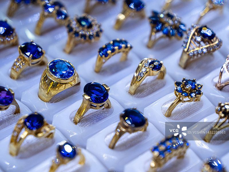 蓝宝石和托帕石彩色宝石戒指，珠宝店陈列。 闪亮彩色宝石和钻石的奢华戒指展示。 高端奢华购物图片素材