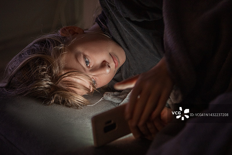 美丽的金色少女在晚上使用智能手机的肖像图片素材
