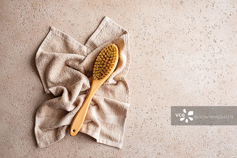 用于干刷按摩的木制身体刷和混凝土背景上的浴巾，俯视图。家庭水疗概念。零浪费。平放。复制空间。图片素材