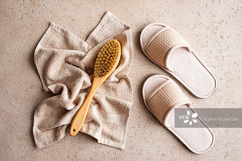 用于干刷按摩的木制身体刷、拖鞋和浴巾在混凝土背景上，俯视图。居家水疗概念。零浪费。平铺。复制空间。图片素材