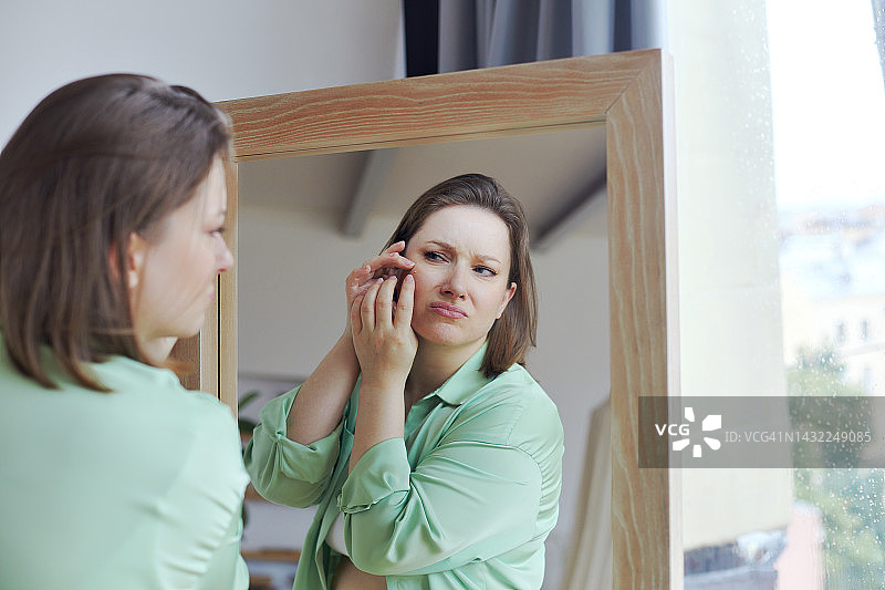 因痤疮烦恼的超重妇女照镜，为肌肤问题感到沮丧图片素材